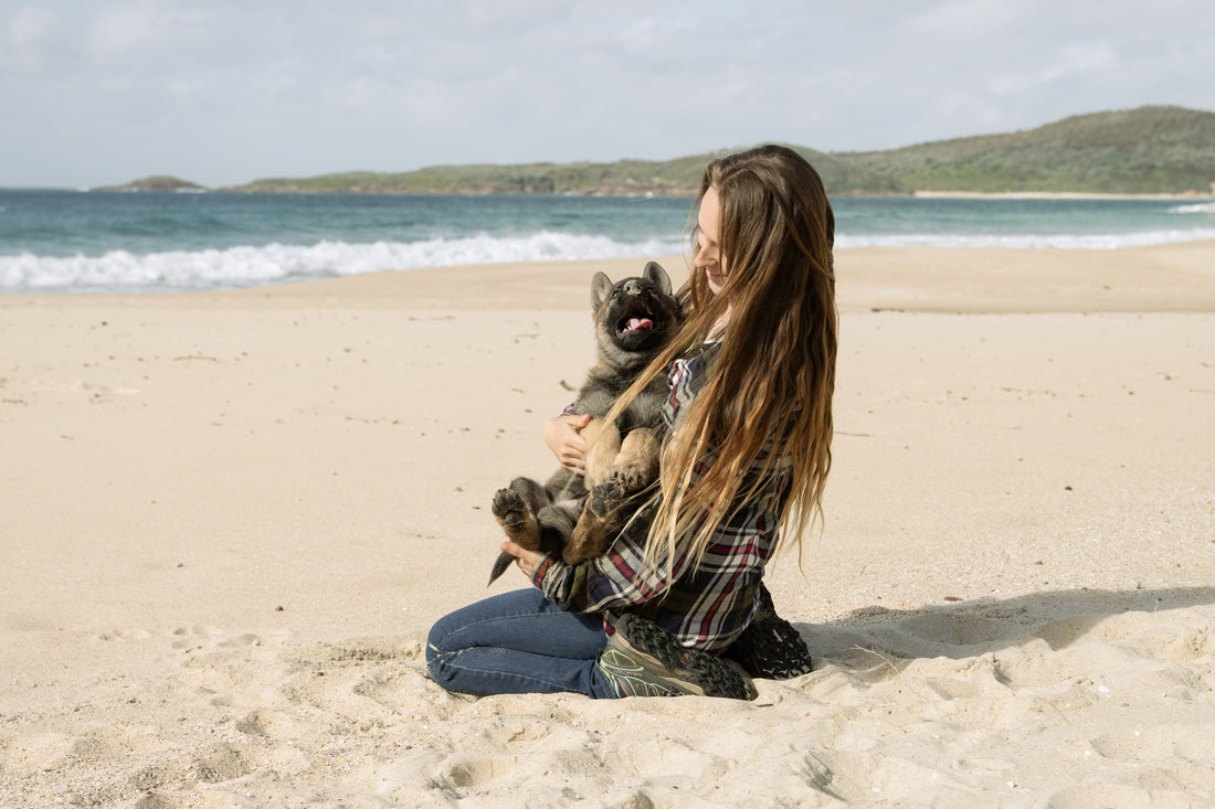 Woman sitting on a beach holding her happy dog and enjoying the outdoors together”